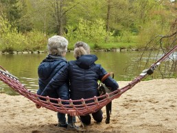 two ladies sitting in hammock looking over a pond and forest of trees