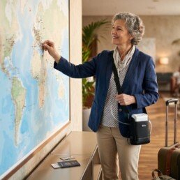 Traveller with a portable oxygen concentrator and suitcase beside a world map, representing medical oxygen support for holidays abroad.